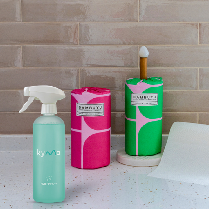 Three cleaning products from Bambuyu  X Kyma cleaning set on a countertop with a tiled wall background.