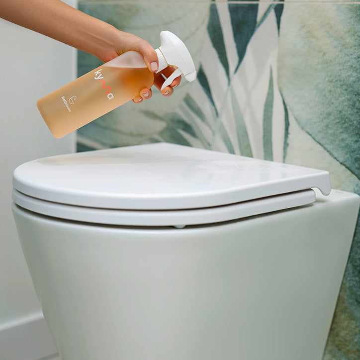 Person using Kyma bathroom cleaner spray bottle to clean a toilet lid.